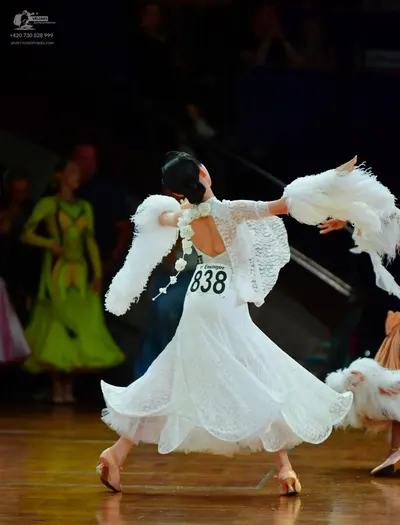 Dancesport competitor: Foreground female dancer: white lace ballgown with large white feathery arm atta