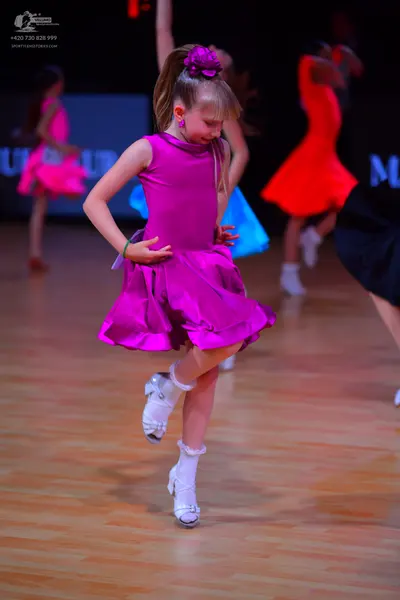 Dancesport competitor: Female dancer in foreground: magenta sleeveless dress with a flared skirt and sa