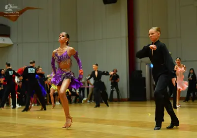 Dancesport competitor: Female dancer in foreground: purple sequined Latin dress with long sleeves and m