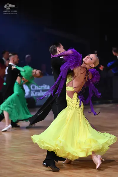 Dancesport competitor: Female dancer in foreground: yellow ballroom dress with purple feather accents a