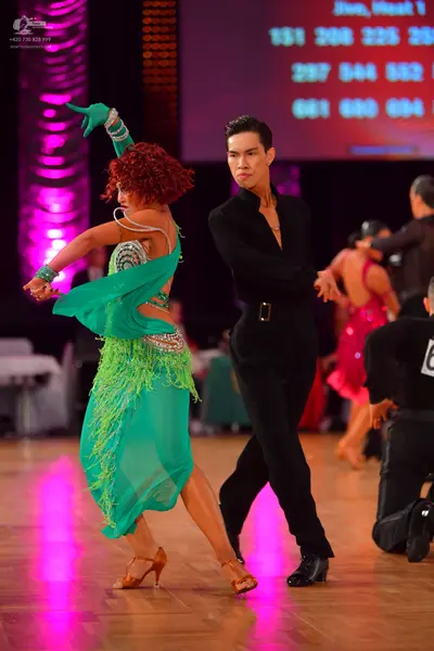 Dancesport competitor: Female dancer in foreground: teal green Latin dress with lime green fringe and s