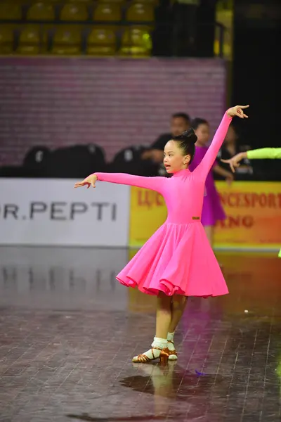 Dancesport competitor: Female dancer: bright pink Latin dress with long sleeves and a flared skirt
