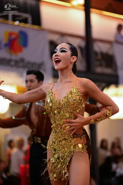 Dancesport competitor: Female dancer: gold latin dress covered in sequins and metallic fringe, with mat