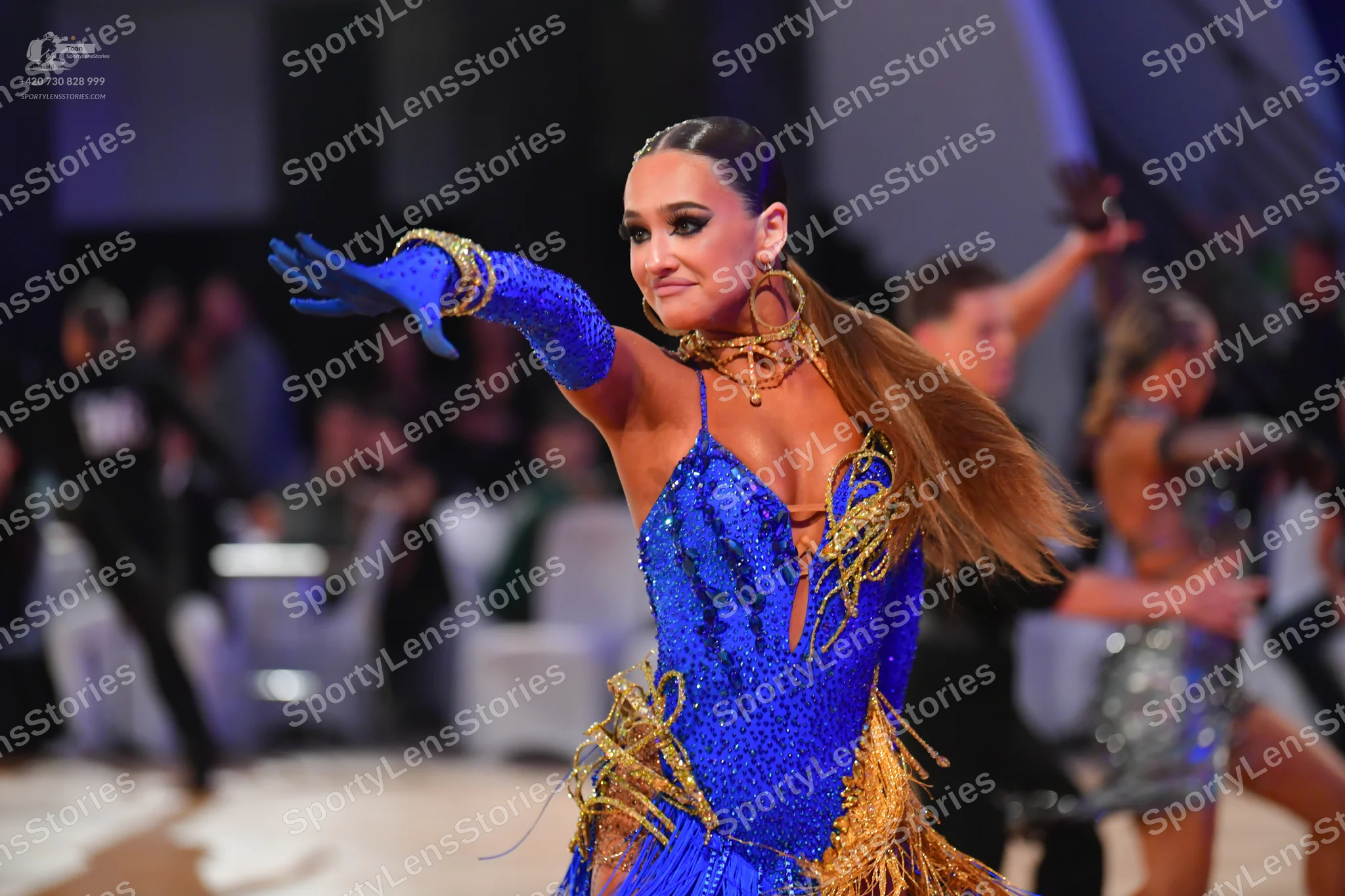 Dancesport competitor: Main female dancer: blue sequined Latin dress with gold fringe, matching long bl