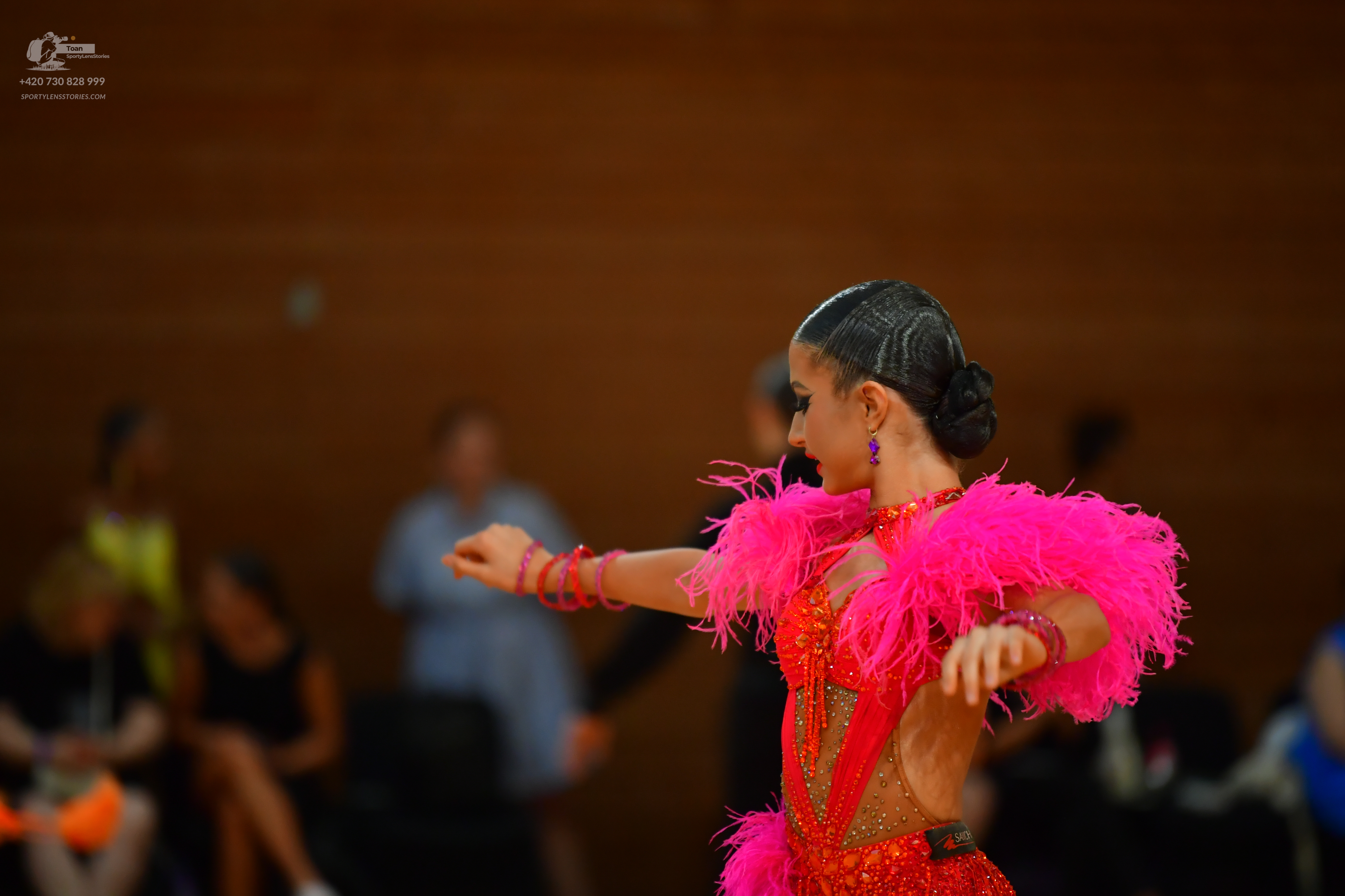 Dancesport competitor: Red latin dress with a plunging V-neckline, sheer long sleeves, and a dramatic, 