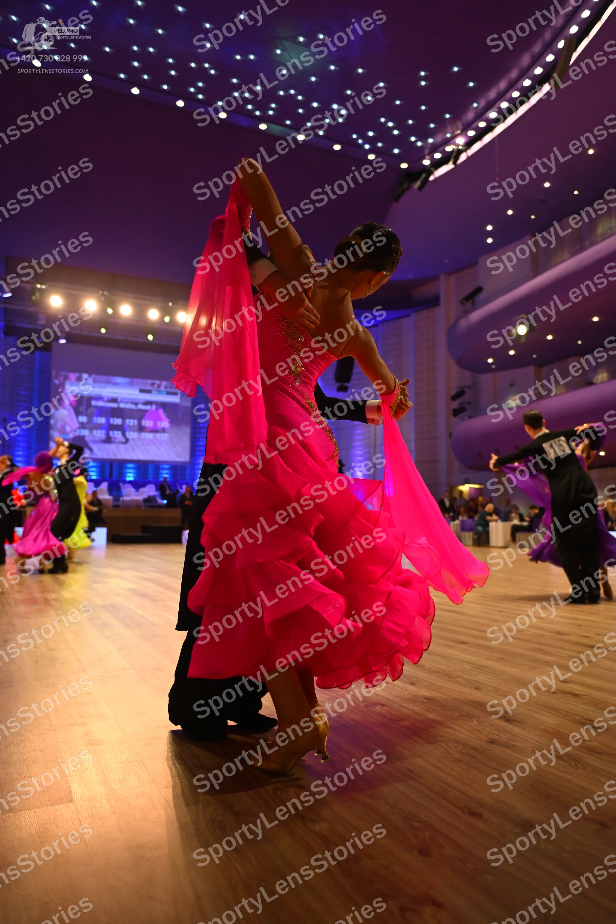 Dancesport competitor: Female dancer in foreground: vibrant pink latin dress with a voluminous, multi-l