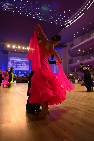 Dancesport competitor: Female dancer in foreground: vibrant pink latin dress with a voluminous, multi-l