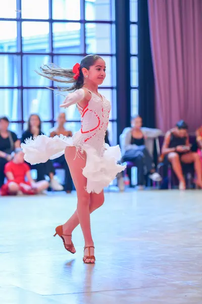 Dancesport competitor: Female dancer: white latin dress with red accents, ruffled skirt, and long sleev