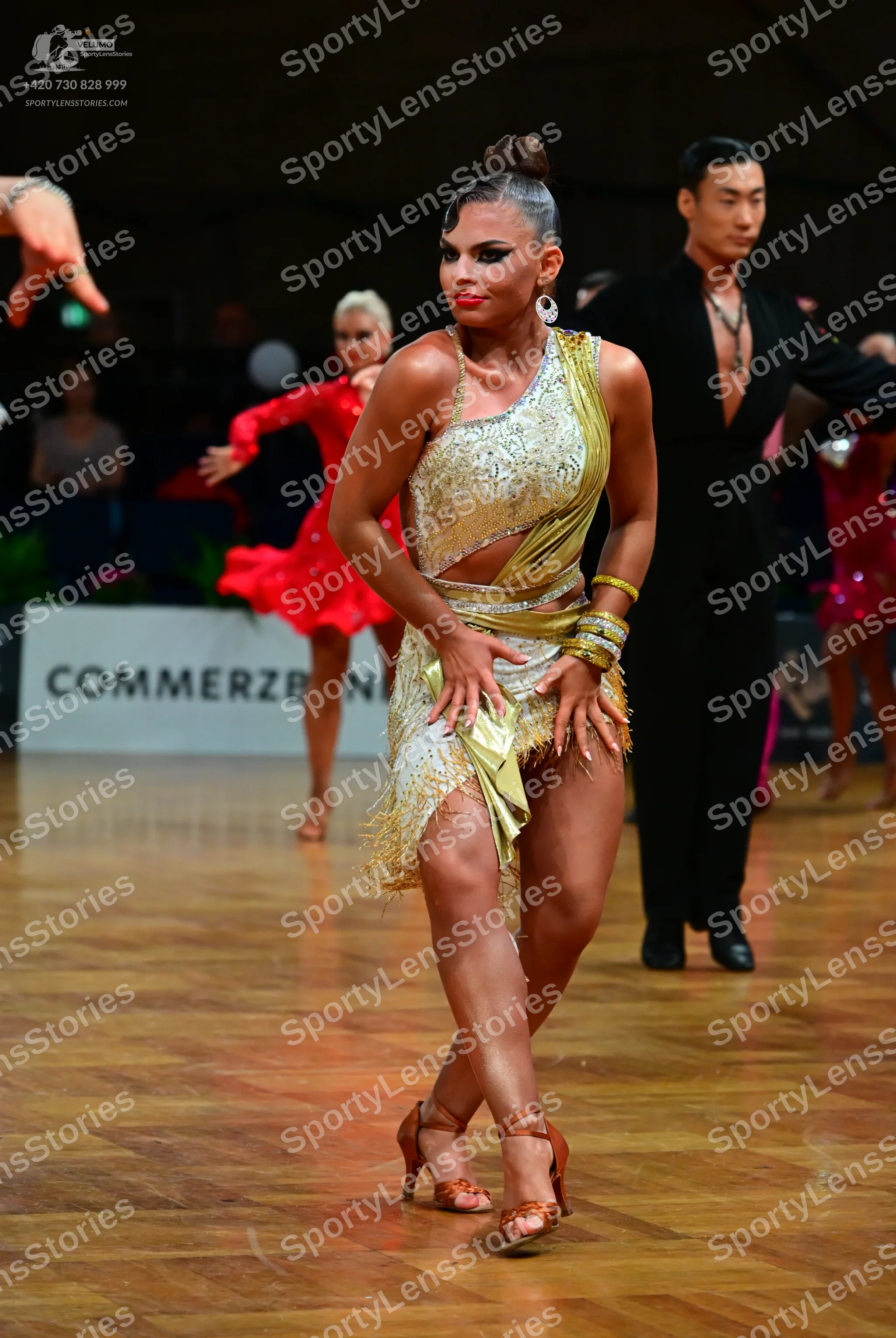 Dancesport competitor: Female dancer in foreground: gold/champagne sequined Latin dress with cutouts an