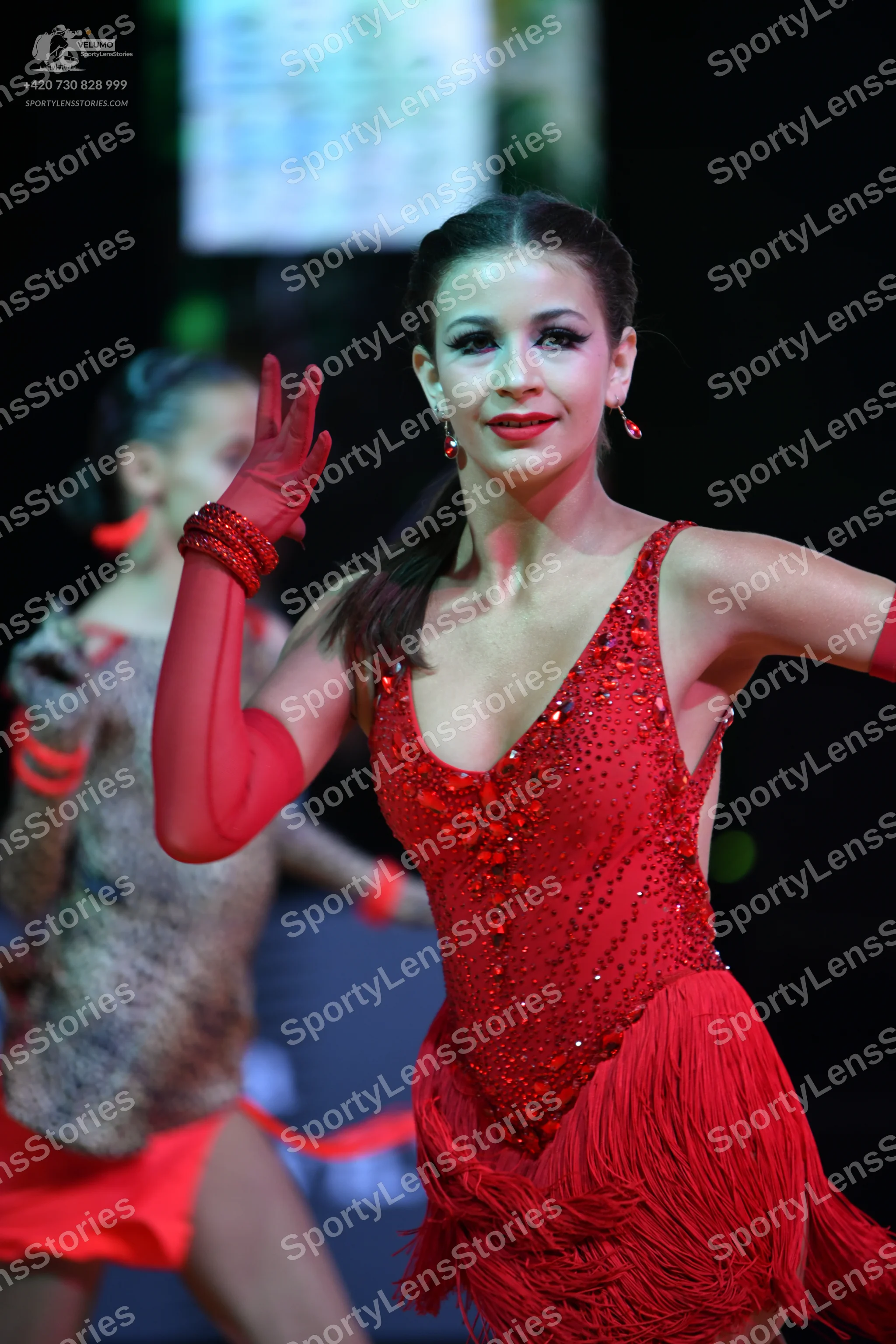 Dancesport competitor: Female dancer in foreground: red latin dress with sequined bodice and fringe ski