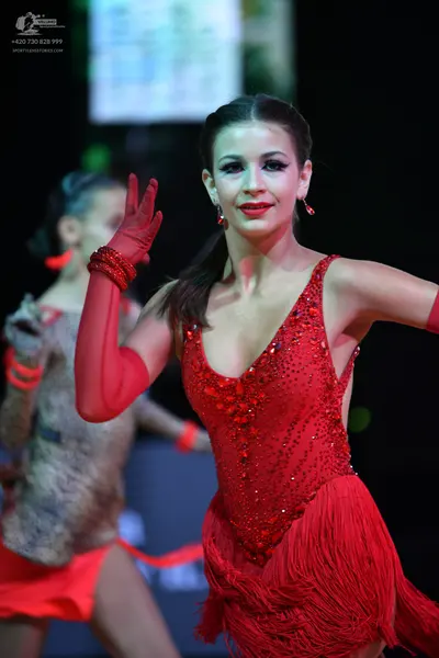 Dancesport competitor: Female dancer in foreground: red latin dress with sequined bodice and fringe ski
