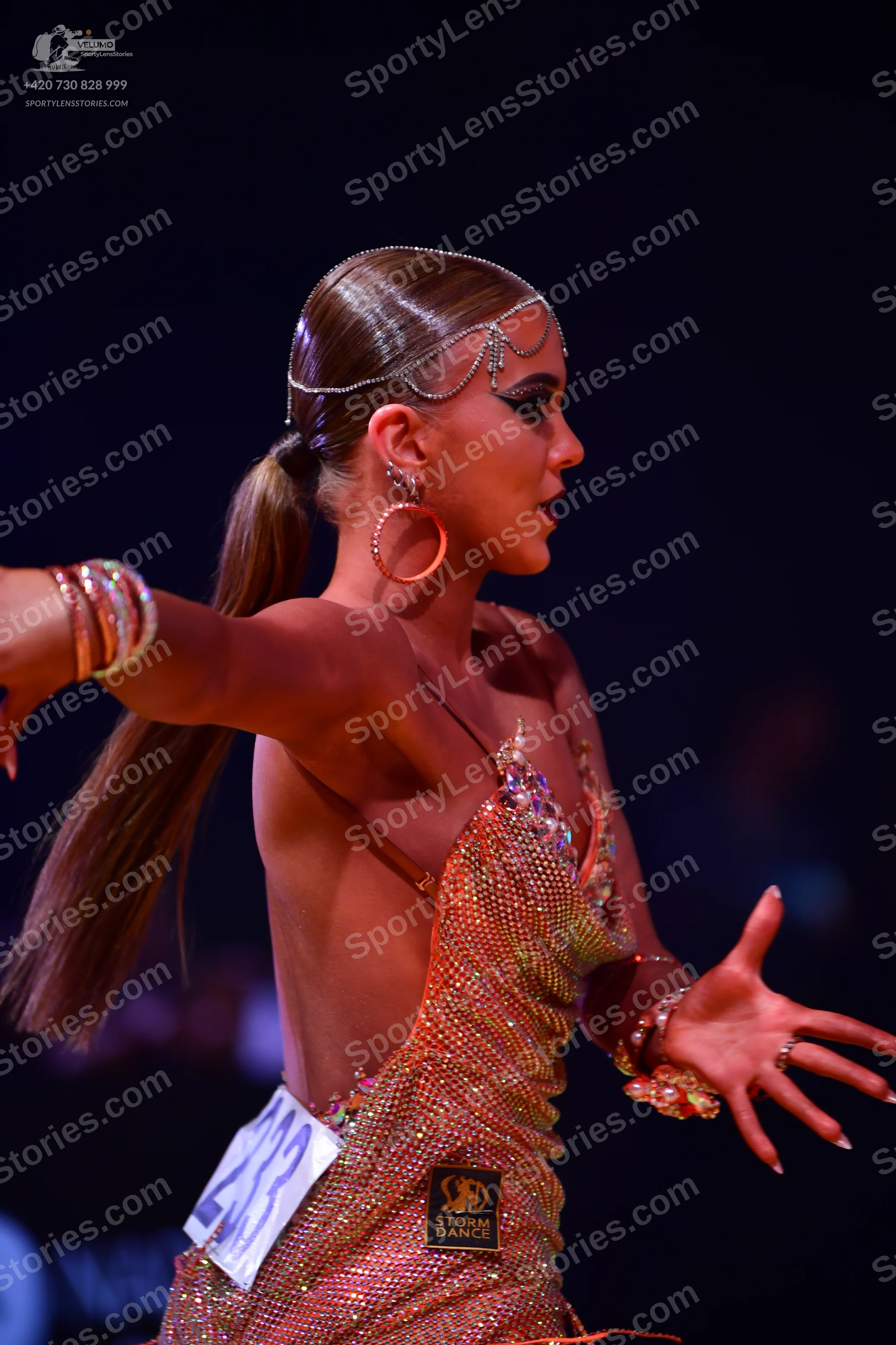Dancesport competitor: Female dancer: gold/bronze sequined Latin dress with thin straps; accessories in