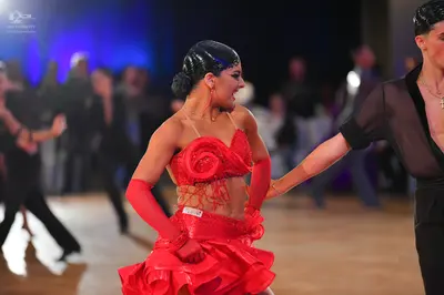 Dancesport competitor: Female dancer: red Latin dress with a large fabric rose on the bodice, a ruffled
