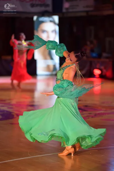 Dancesport competitor: Female dancer in foreground: green ballgown with a sequined bodice and large, fl