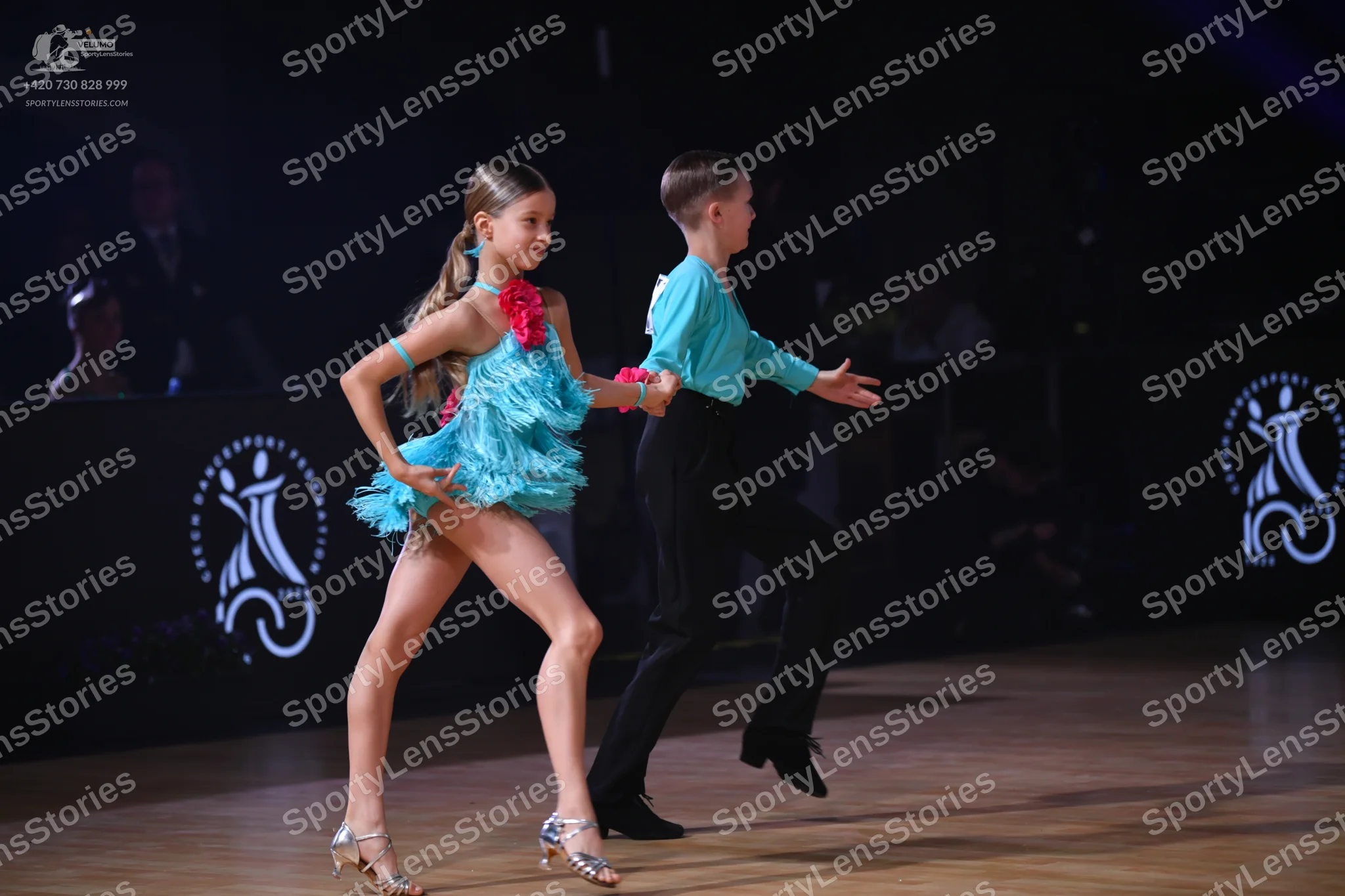 Dancesport competitor: Female dancer: light blue latin dress with fringe and a pink flower accessory on