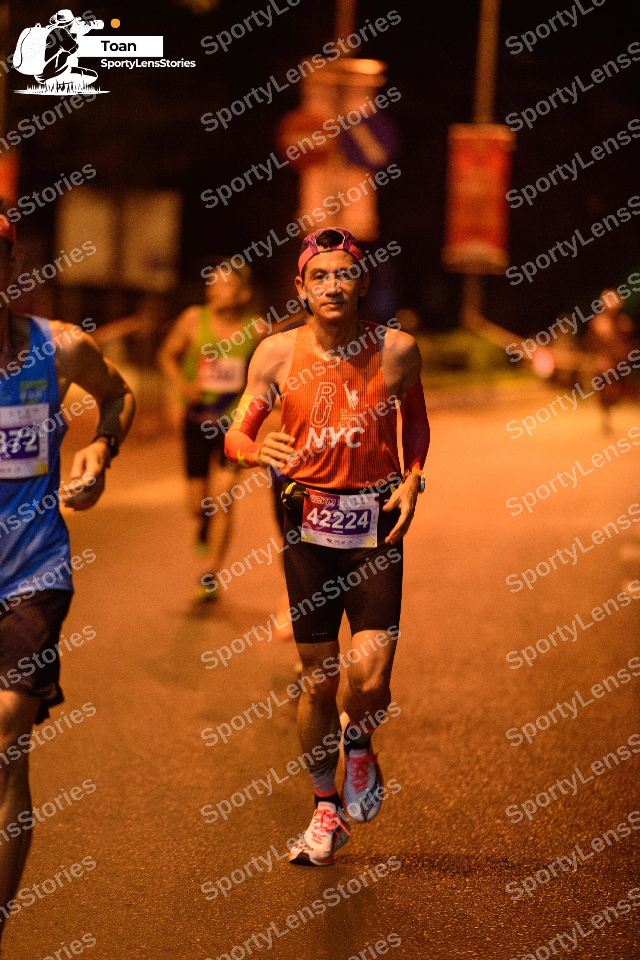 Marathon runner #372, #42224: Runner 1: orange tank top, black shorts, white and grey running shoes, pink head