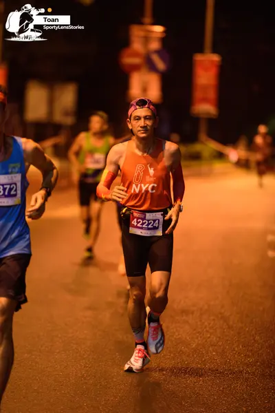 Marathon runner #372, #42224: Runner 1: orange tank top, black shorts, white and grey running shoes, pink head