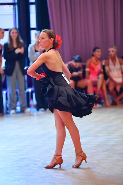 Dancesport competitor: Main dancer: black latin dress with a ruffled skirt, a red flower in her hair, a