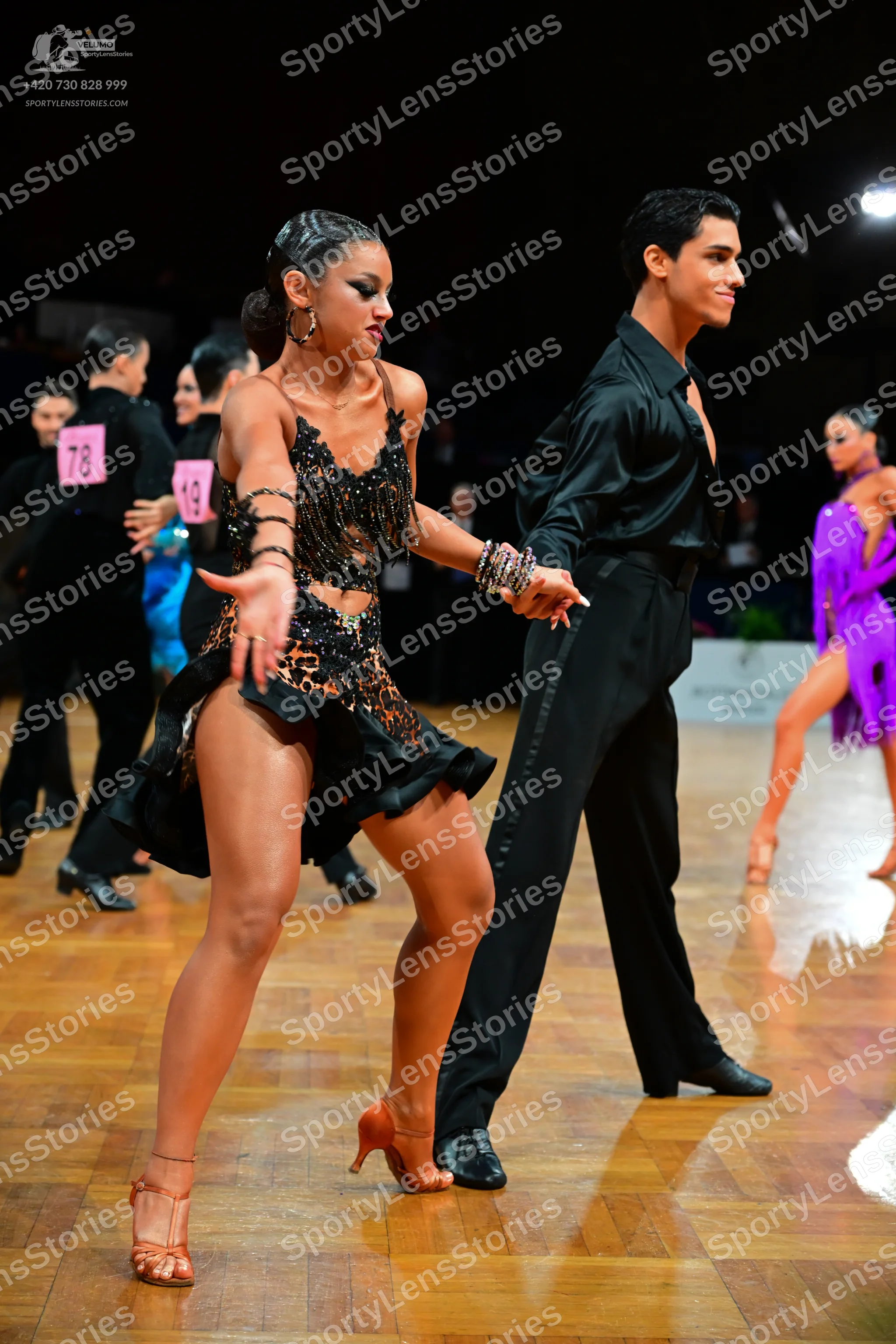 Dancesport competitor #78, #19: Female dancer (foreground): black sequined Latin dress with a ruffled hem and ma
