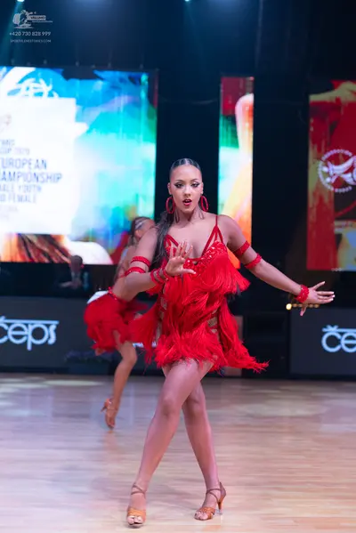Dancesport competitor: Female dancer in foreground: red latin dress with fringe, red armbands, and red 