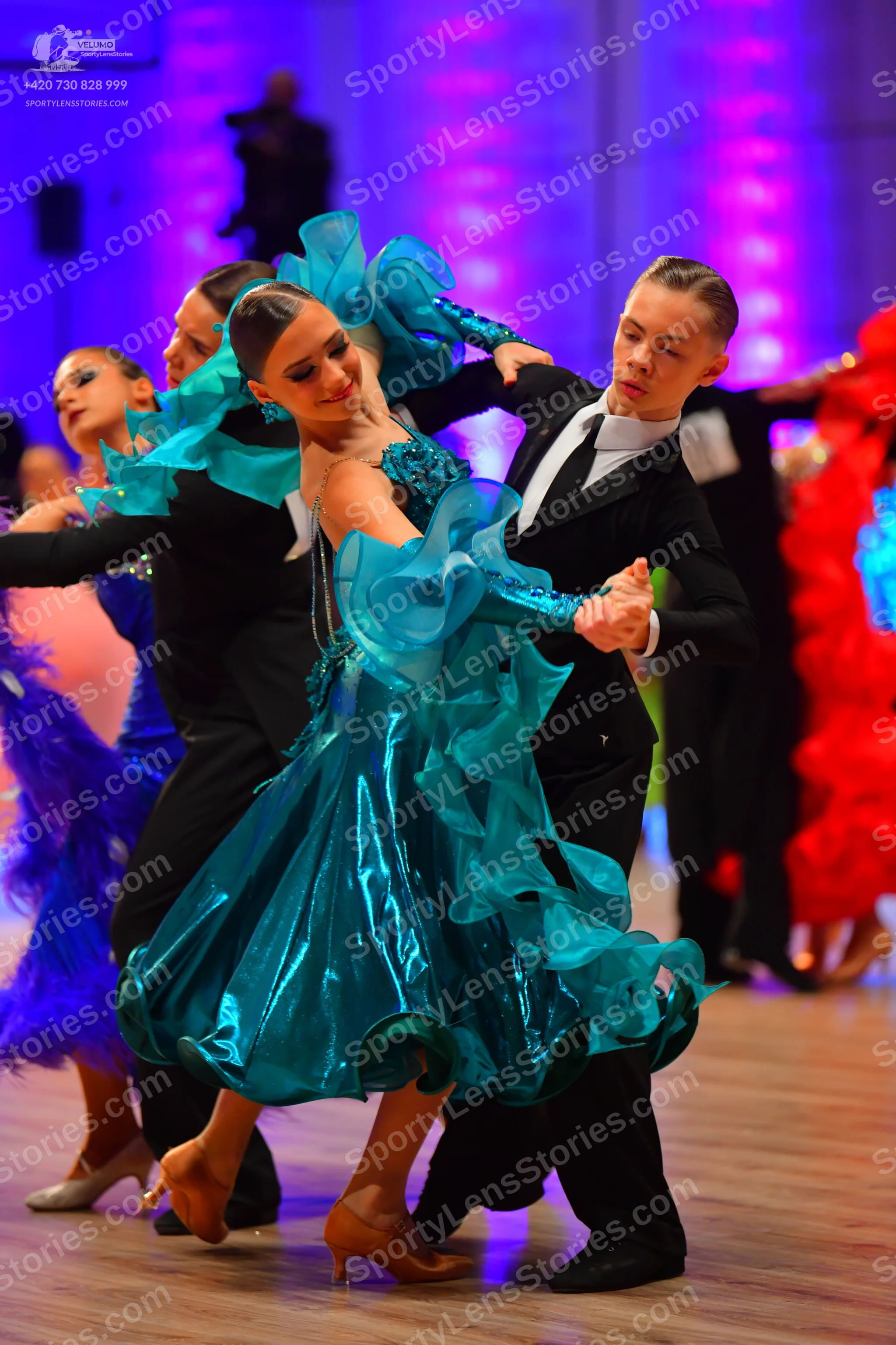 Dancesport competitor: Female dancer: teal satin latin dress with large, voluminous ruffles and sparkli