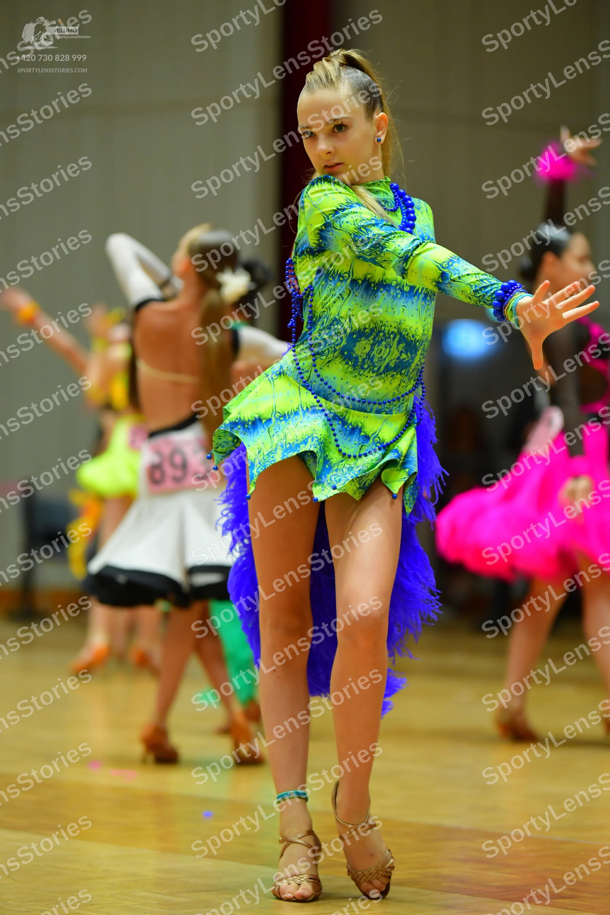 Dancesport competitor #893: Female dancer in foreground: lime green and blue patterned long-sleeved latin dr