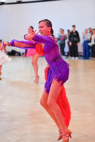 Dancesport competitor: Female dancer in foreground: purple Latin dance dress with long sleeves, purple 