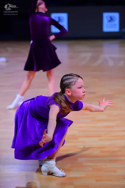 Dancesport competitor: Female dancer in foreground: bright purple short-sleeved dress with a flared ski