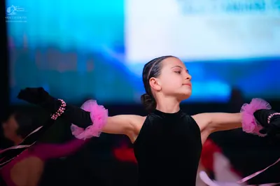 Dancesport competitor: Female dancer: black, long-sleeved, high-neck bodysuit with pink ruffled fabric 