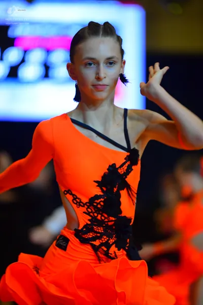 Dancesport competitor: Female dancer: orange latin dress with one long sleeve, black lace/appliqué deta