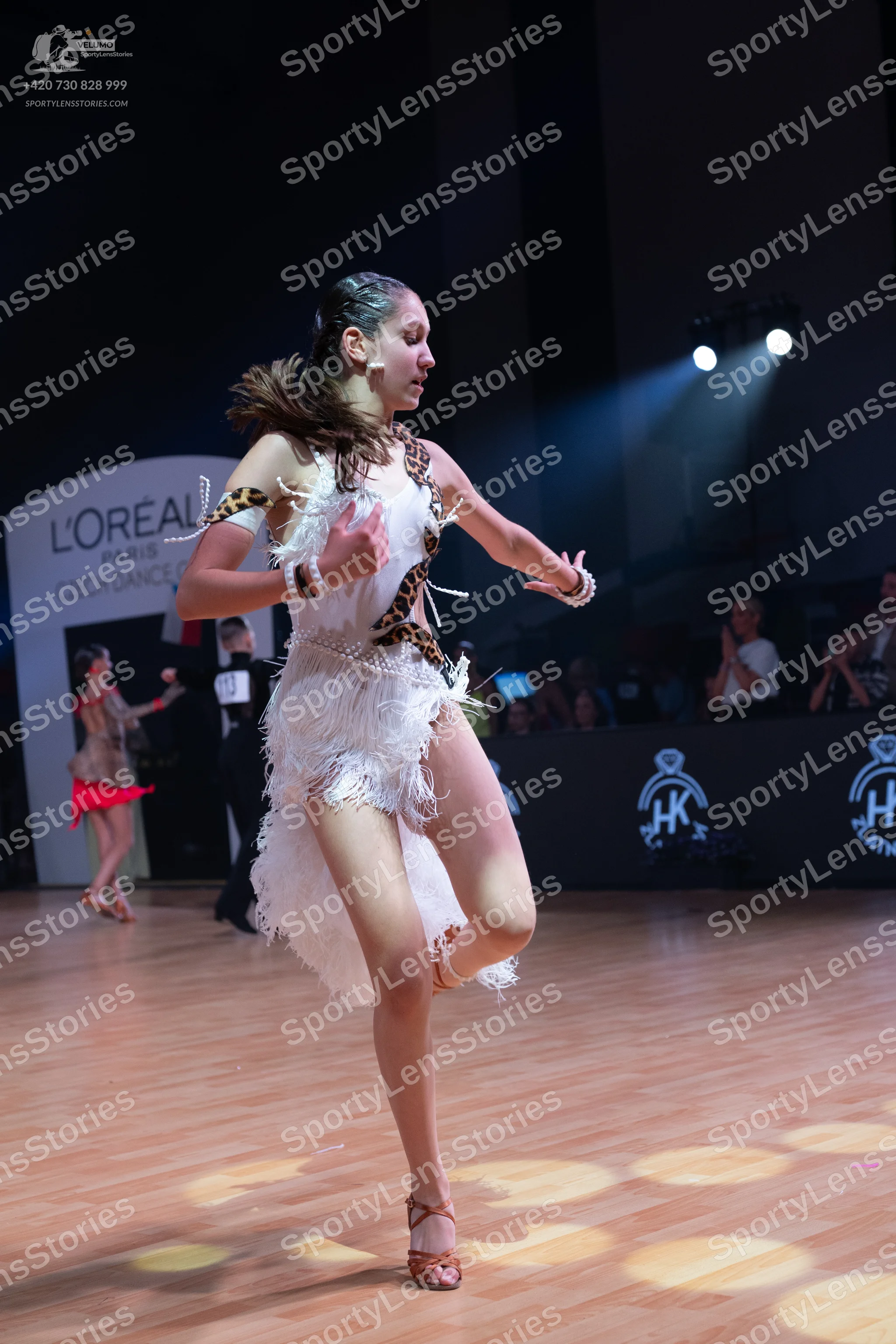Dancesport competitor: Female dancer (foreground): white latin dress with leopard print trim and long w