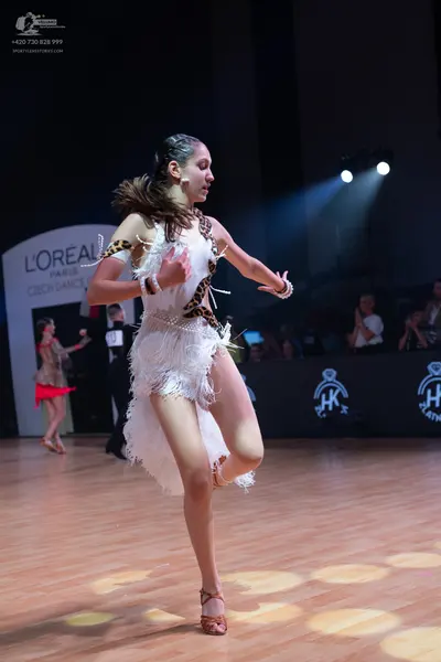 Dancesport competitor: Female dancer (foreground): white latin dress with leopard print trim and long w