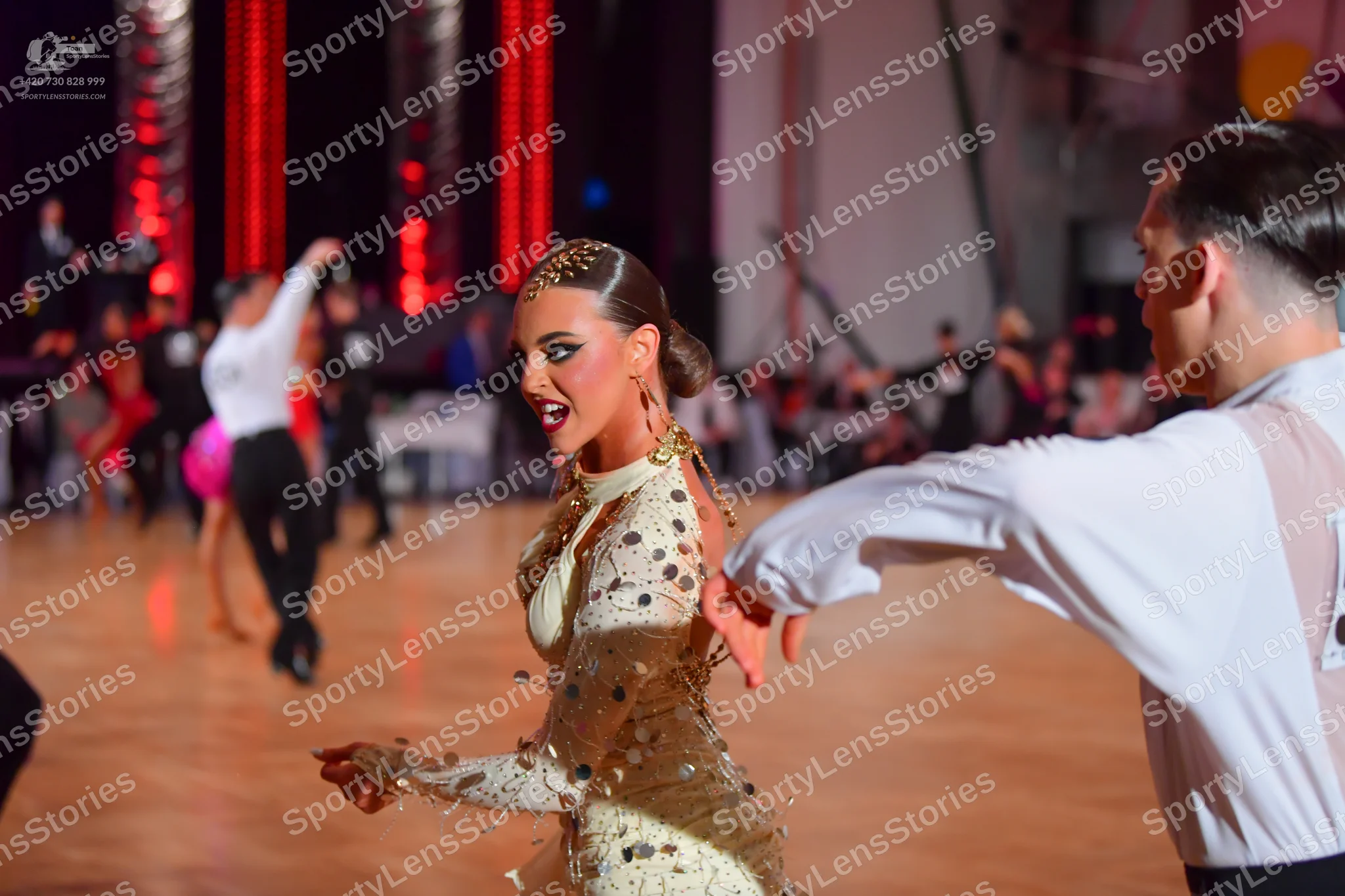 Dancesport competitor: Female dancer in foreground: cream-colored, long-sleeved Latin dress with large,