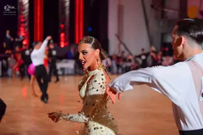 Dancesport competitor: Female dancer in foreground: cream-colored, long-sleeved Latin dress with large,