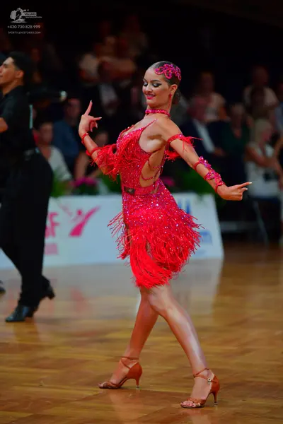 Dancesport competitor: Female dancer: red Latin dress with fringe and sequins, matching red arm bands a
