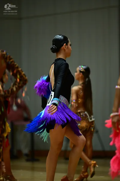 Dancesport competitor: Female dancer in foreground: black long-sleeved latin dress with purple, blue, a