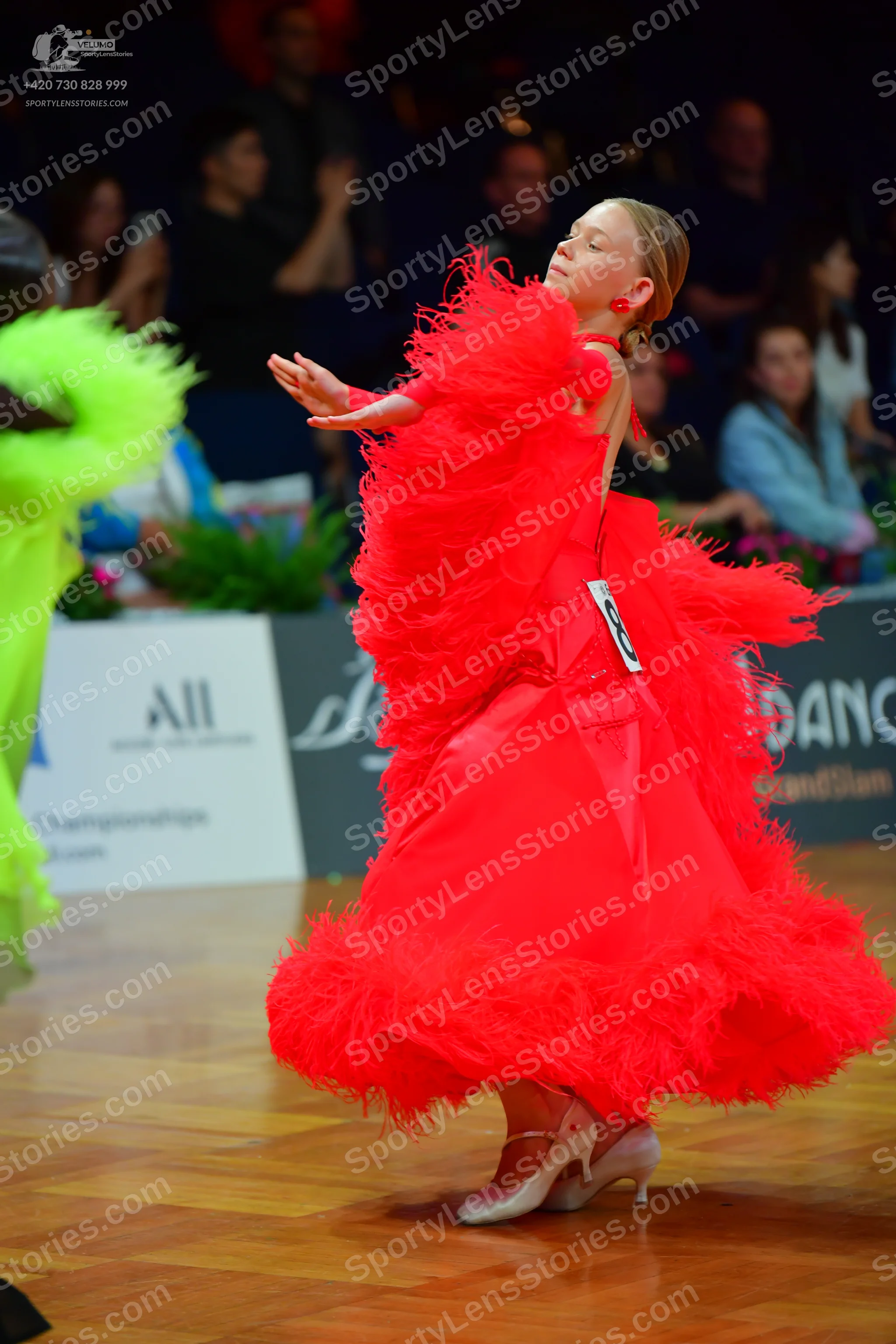 Dancesport competitor: Female dancer in focus: red latin dress with voluminous red feather fringe aroun