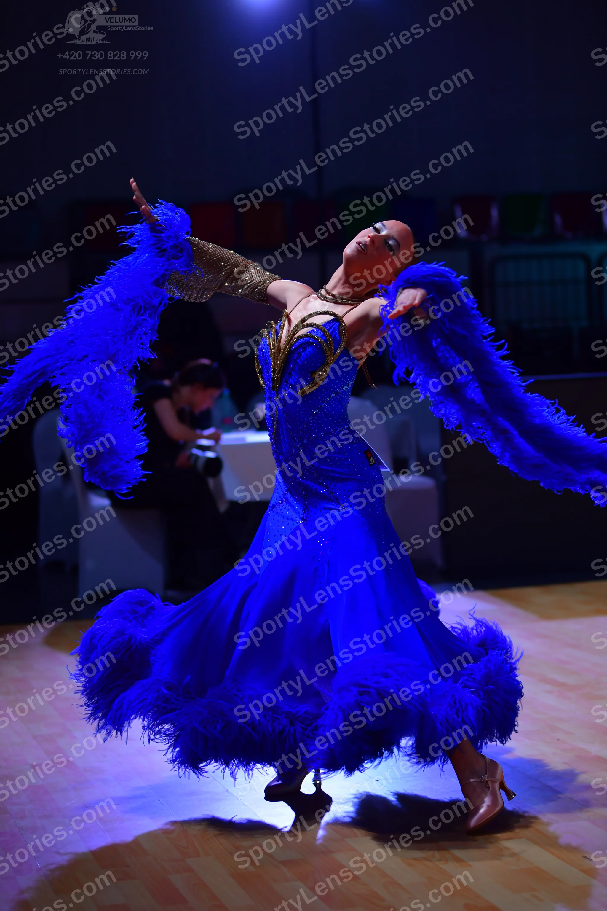 Dancesport competitor: Female dancer: blue ballgown with blue feathers on the skirt and sleeves, and a 
