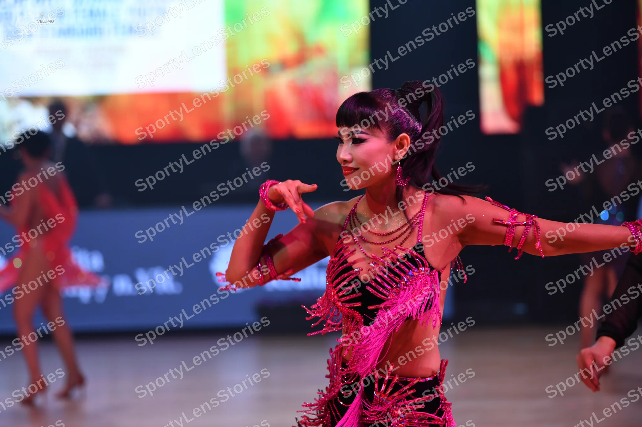 Dancesport competitor: Female dancer in foreground: black and pink latin costume with heavy pink fringe