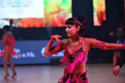 Dancesport competitor: Female dancer in foreground: black and pink latin costume with heavy pink fringe