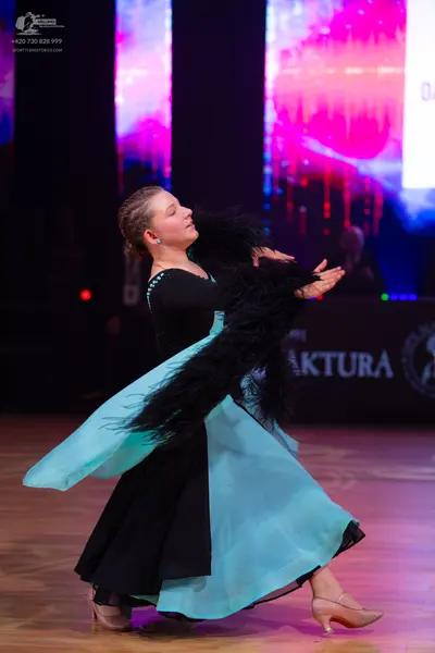 Dancesport competitor: Female dancer: black and light blue ballroom gown with a large, flowing turquois
