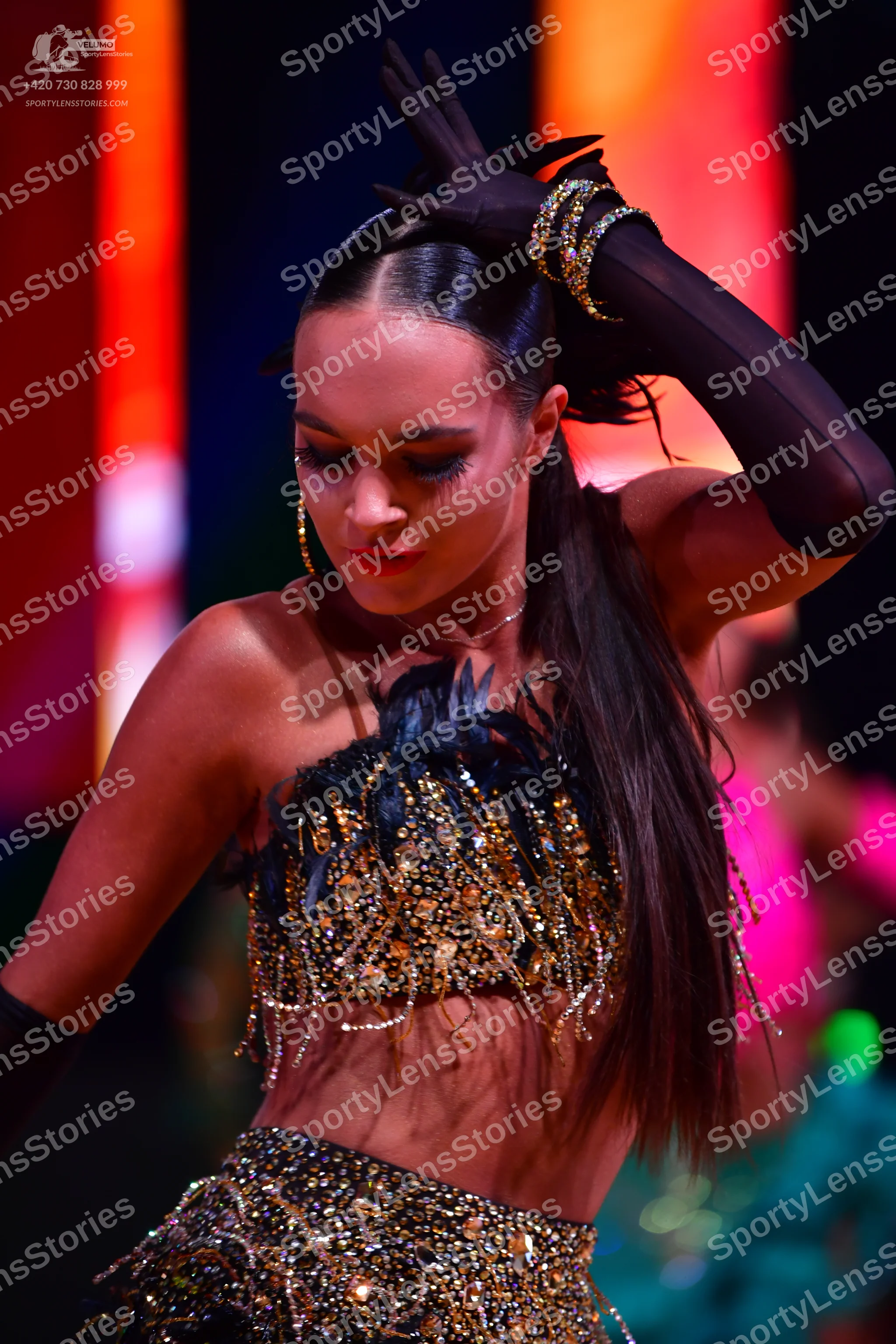 Dancesport competitor: Female dancer: dark two-piece latin costume heavily embellished with gold and si