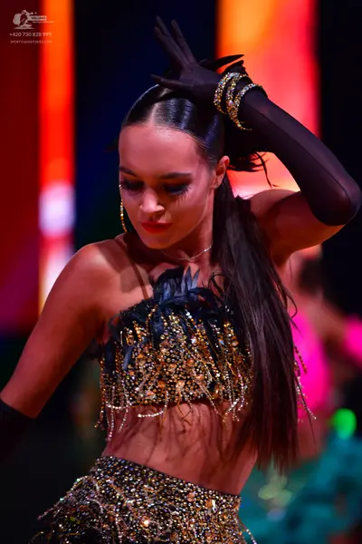 Dancesport competitor: Female dancer: dark two-piece latin costume heavily embellished with gold and si