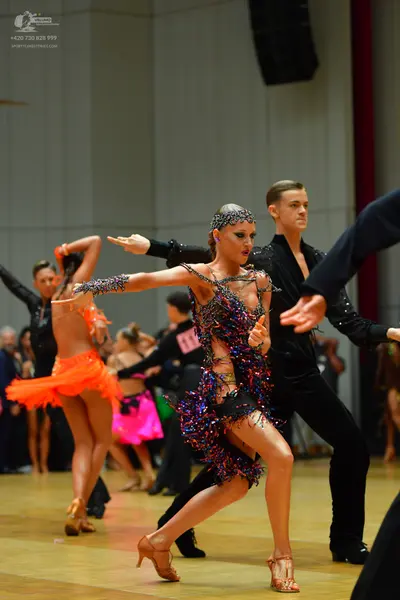 Dancesport competitor: Female dancer in foreground: colorful latin dress covered in blue, purple, red, 