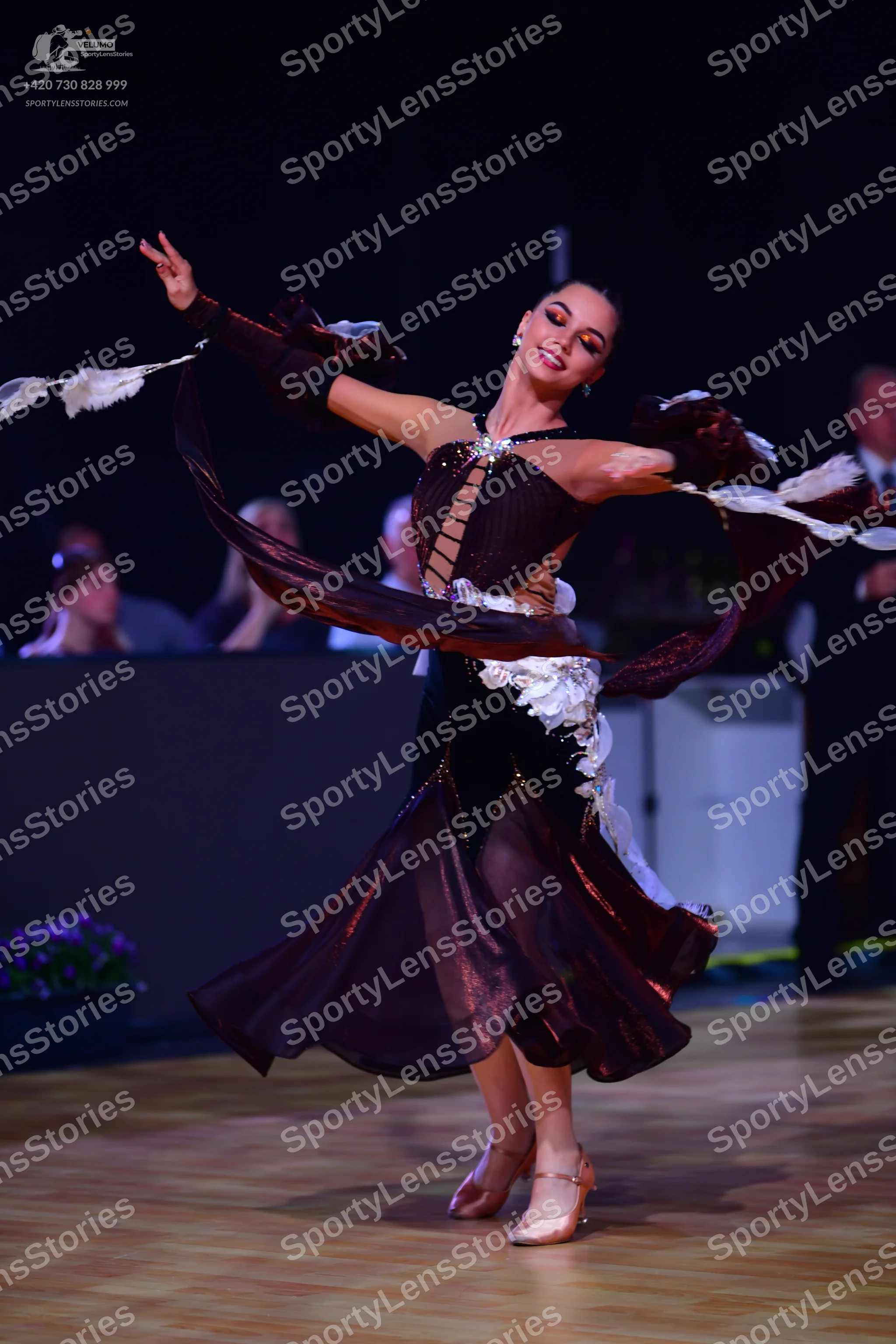 Dancesport competitor: Female dancer: dark brown Latin dance dress with flowing sheer fabric, white flo