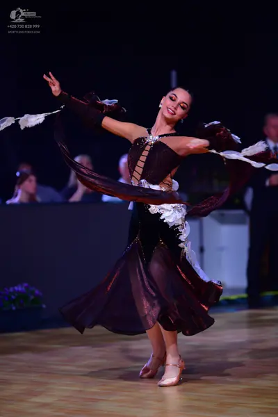 Dancesport competitor: Female dancer: dark brown Latin dance dress with flowing sheer fabric, white flo