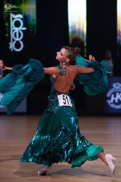 Dancesport competitor: Female dancer: dark teal, metallic-finish ballgown with an open back and large, 
