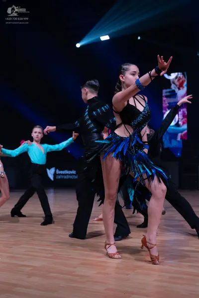 Dancesport competitor: Female dancer in foreground: black latin dress with blue and black feather-like 