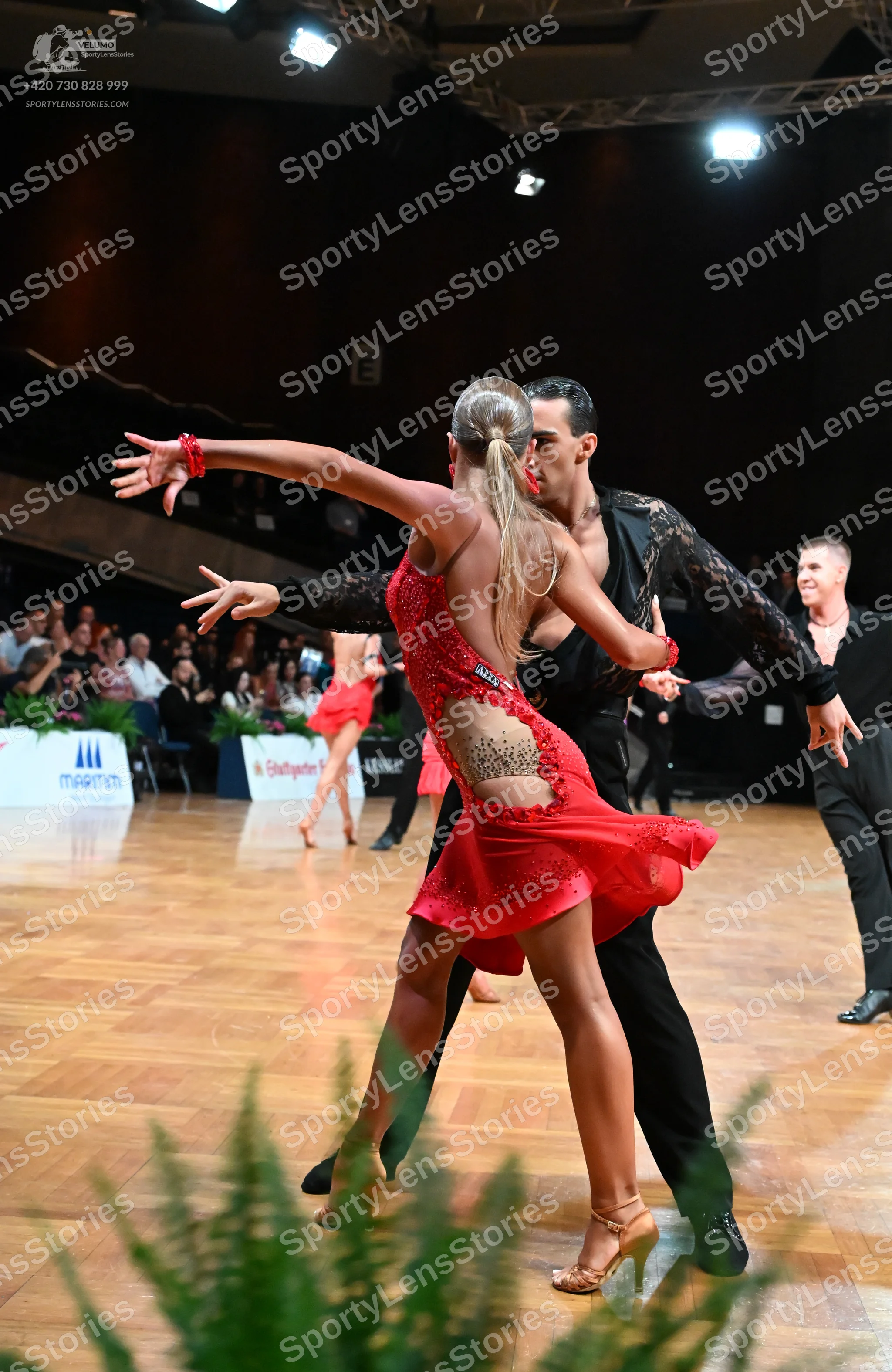Dancesport competitor: Female dancer in foreground: red Latin dress with sequins and mesh/lace detailin