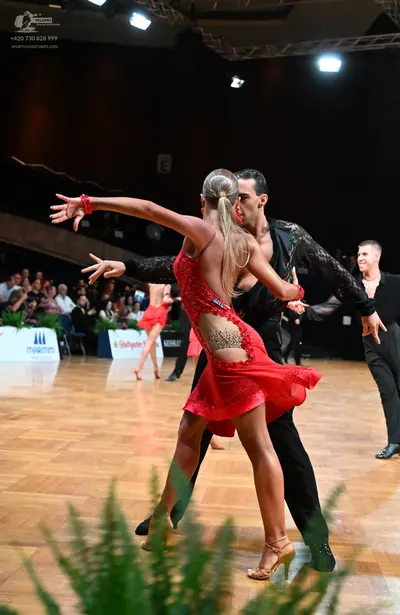 Dancesport competitor: Female dancer in foreground: red Latin dress with sequins and mesh/lace detailin